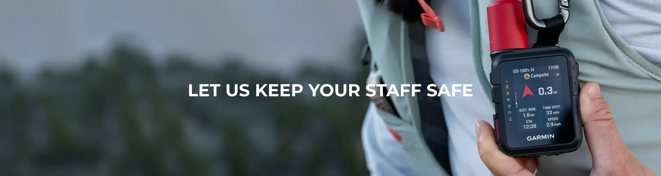 Close-up of a Garmin handheld GPS device held in a hand, with 'LET US KEEP YOUR STAFF SAFE' text across a blurred outdoor background.